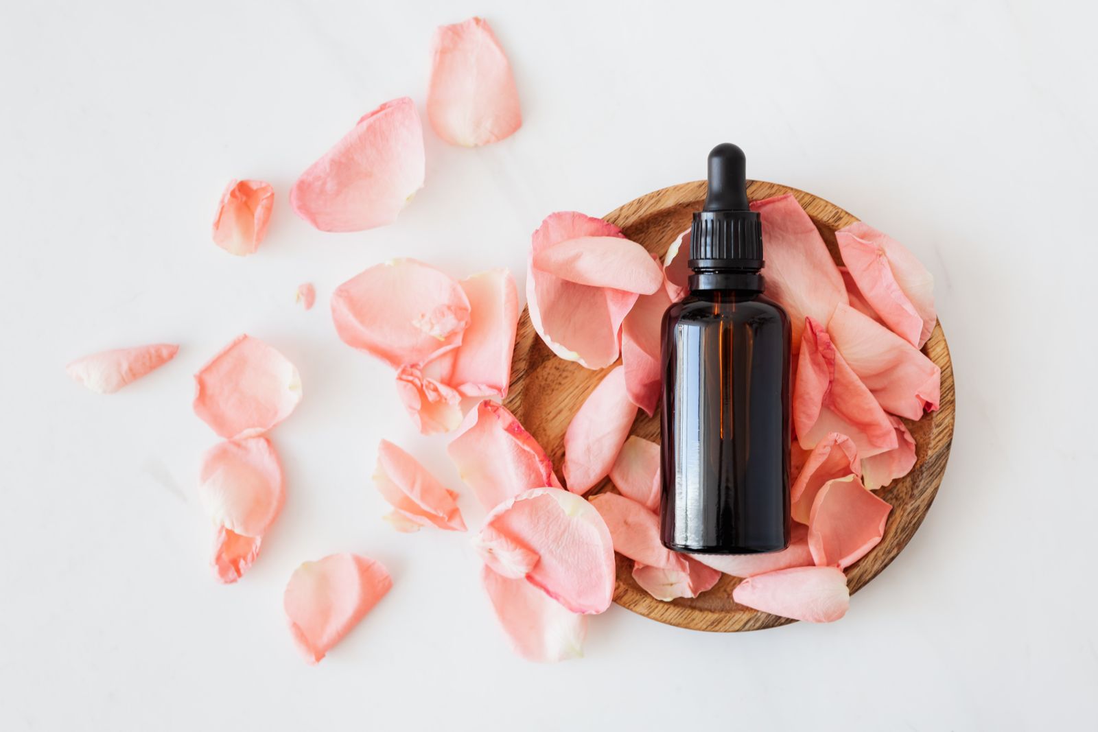 Unbranded amber skincare serum dropper bottle on white linen with rose petals